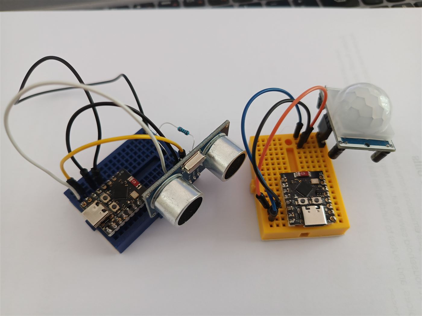 Two ESP32-C3 boards on mini breadboards, one wired to an ultrasonic sensor and one to a PIR motion sensor